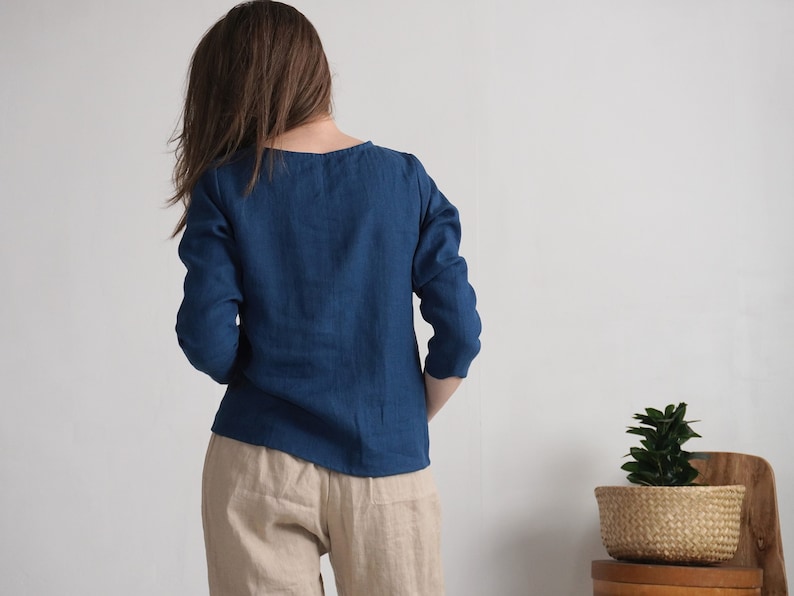 May include: A long-sleeved, deep blue top with a simple round neckline, paired with light beige trousers. The top features a straight hemline and a solid color finish, while the trousers have a relaxed fit and a neutral, light tan appearance.