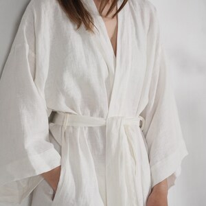 May include: A white linen robe with a long, flowing silhouette and a tie belt. The robe has a relaxed, comfortable fit and is perfect for lounging around the house.