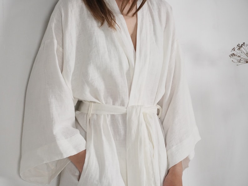 May include: A white linen robe with a long, flowing silhouette and a tie belt. The robe has a relaxed, comfortable fit and is perfect for lounging around the house.