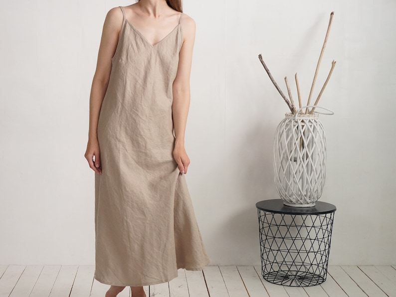 Op de afbeelding: Een beige enkellange slipdress met een V-hals en dunne spaghettibandjes. Het kledingstuk heeft een los, recht model dat tot op de enkels valt en is gemaakt van een effen stof met een zichtbare, natuurlijke weefstructuur.
