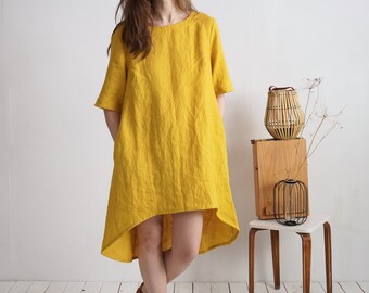 Peut inclure: Une robe jaune moutarde avec une encolure ronde, des manches courtes et un ourlet asymétrique. Le vêtement présente une coupe ample et décontractée avec des poches latérales, tombant au-dessus des genoux devant et plus long derrière.