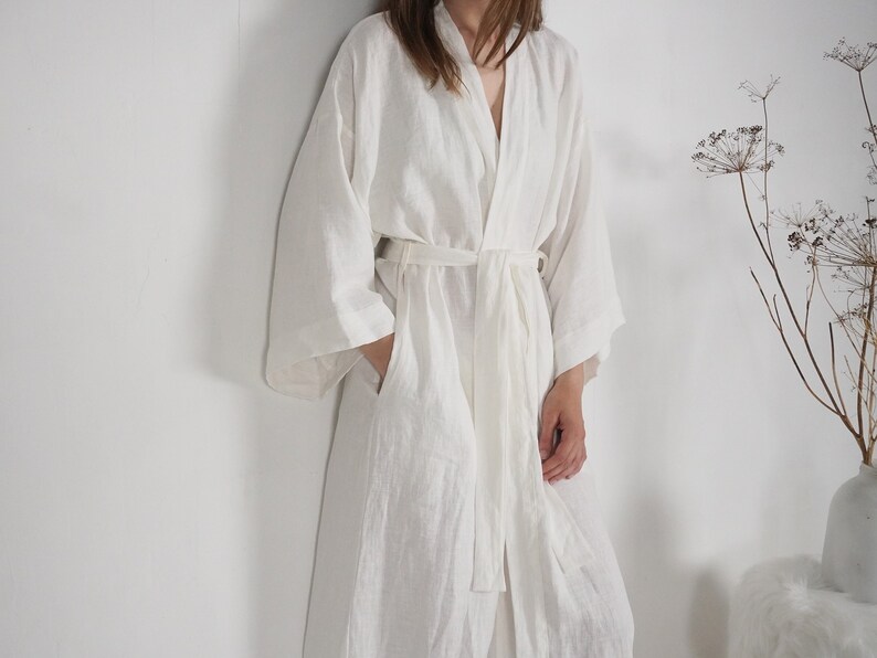 May include: A white linen robe with a long, flowing silhouette and a sash tie at the waist.