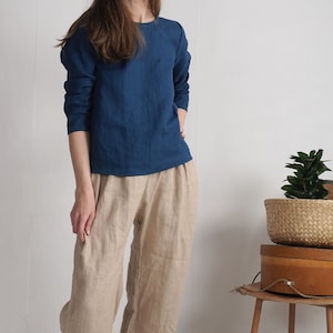 May include: A long-sleeved dark blue top with a round neckline paired with loose-fitting beige trousers. The top features a straight hemline and the trousers have a relaxed fit with a visible seam down the center of each leg.