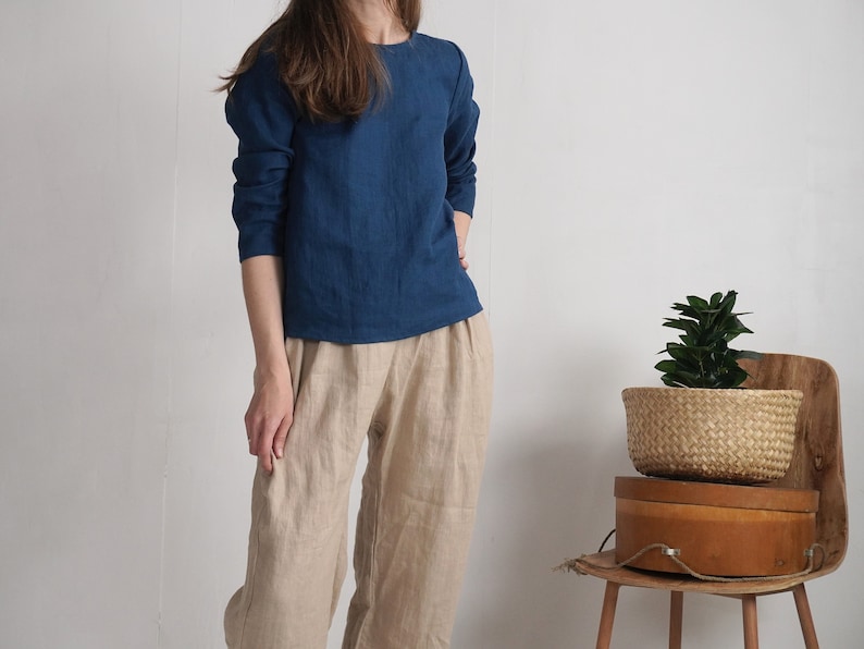 May include: A long-sleeved dark blue top with a round neckline paired with loose-fitting beige trousers. The top features a straight hemline and the trousers have a relaxed fit with a visible seam down the center of each leg.