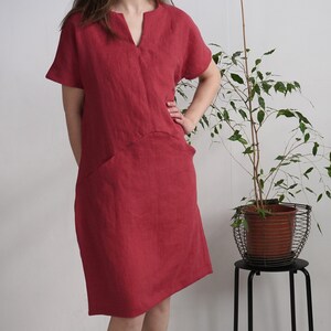 Peut inclure: Une robe en lin rouge avec un col en V et des manches courtes. La robe a une coupe ample et une forme l&eacute;g&egrave;rement trap&egrave;ze. Elle est dot&eacute;e d'une seule poche plaqu&eacute;e sur le c&ocirc;t&eacute; gauche.