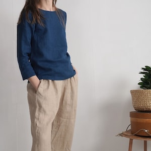 May include: A long-sleeved, solid dark blue top with a round neckline paired with loose-fitting, light beige trousers. The top features three-quarter length sleeves, while the trousers have a relaxed silhouette with visible side pockets.
