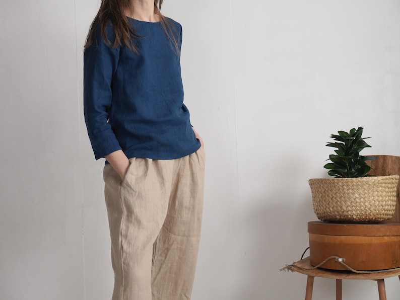 May include: A long-sleeved, solid dark blue top with a round neckline paired with loose-fitting, light beige trousers. The top features three-quarter length sleeves, while the trousers have a relaxed silhouette with visible side pockets.