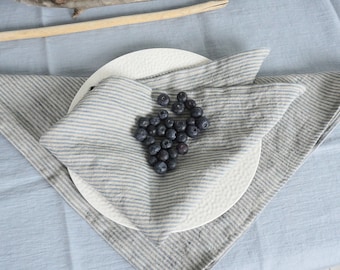 May include: Two blue and white striped linen napkins folded on a white plate with a pile of blueberries in the center.