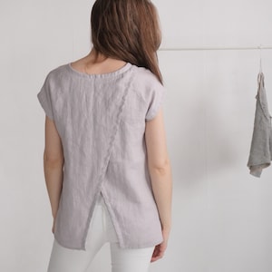 Könnte beinhalten: Ein helllilafarbenes Leinenoberteil mit einem einzigartigen Kreuzrücken-Design und kurzen Ärmeln.