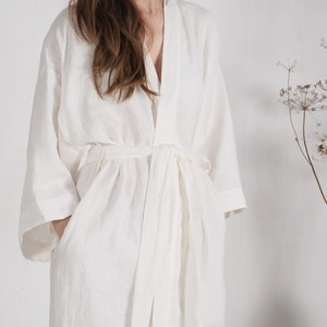 May include: A white linen robe with a long, flowing silhouette and a tie belt. The robe has a relaxed, comfortable fit and is perfect for lounging around the house.