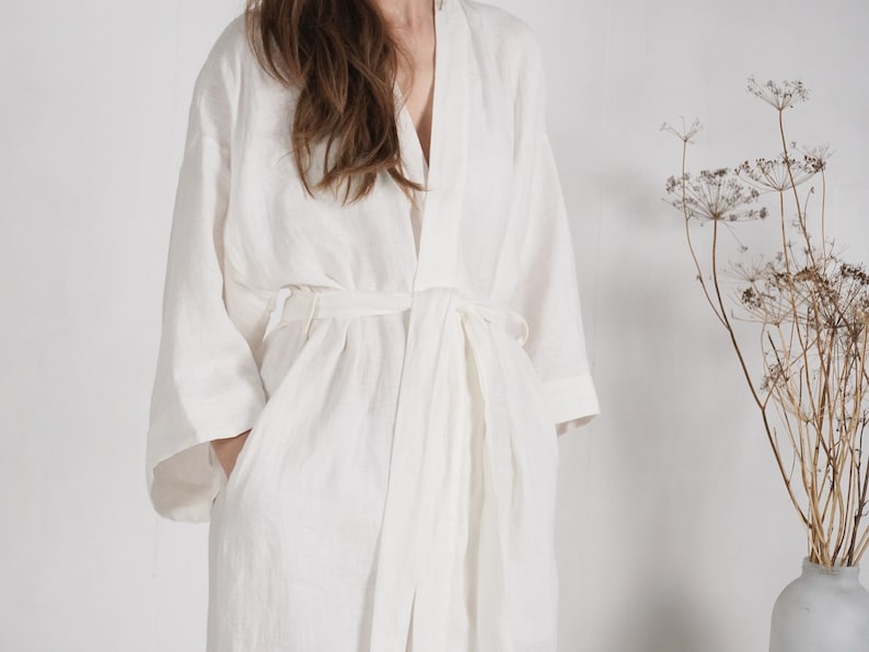 May include: A white linen robe with a long, flowing silhouette and a tie belt. The robe has a relaxed, comfortable fit and is perfect for lounging around the house.
