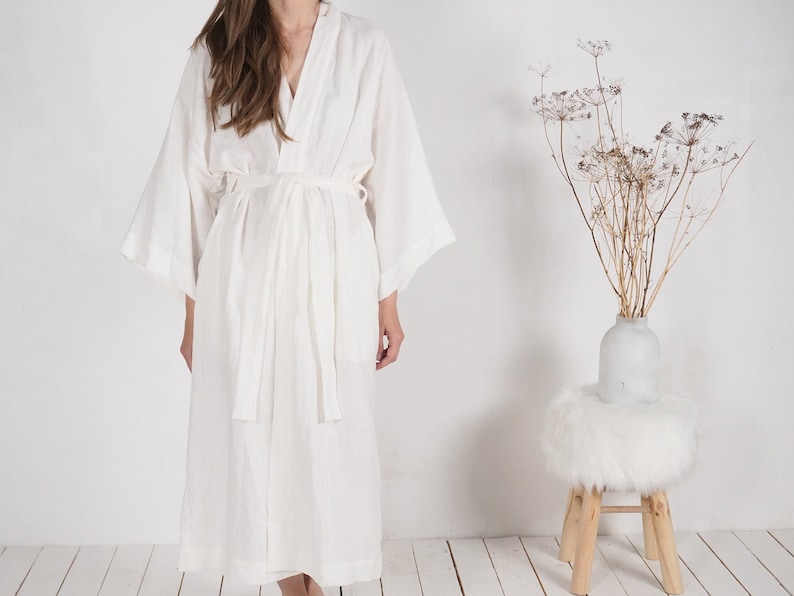 May include: A white linen robe with long sleeves and a tie belt. The robe is loose-fitting and has a relaxed, comfortable look.