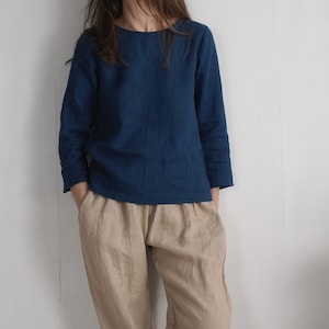 May include: A long-sleeved dark blue top with a round neckline paired with loose-fitting beige trousers. The top features a simple, straight-cut design, while the trousers have a relaxed fit with visible pockets at the sides of the waist.