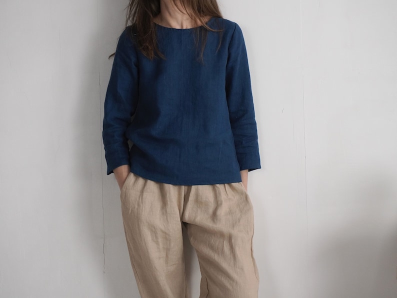 May include: A long-sleeved dark blue top with a round neckline paired with loose-fitting beige trousers. The top features a simple, straight-cut design, while the trousers have a relaxed fit with visible pockets at the sides of the waist.