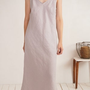 Puede incluir: Un vestido tipo lencero largo hasta los pies, de color gris lavanda claro y confeccionado en tela texturizada. La prenda presenta un escote en V sencillo y tirantes finos y delicados. La silueta es recta, holgada y llega a los tobillos.