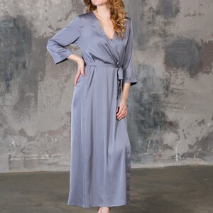 May include: A long, gray satin robe with a V-neck and a tie belt. The robe is worn by a person with long, curly hair.