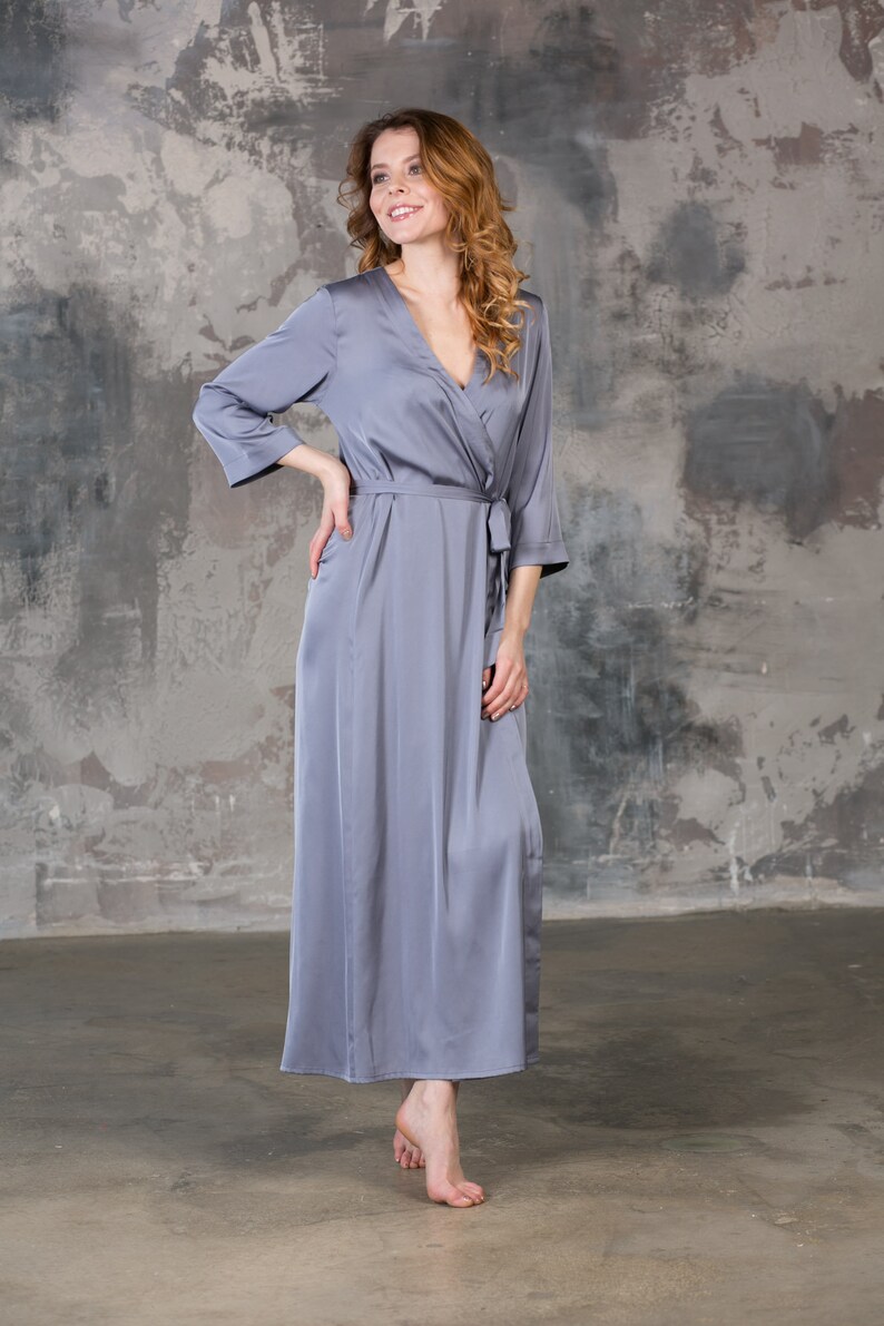 May include: A long, gray satin robe with a V-neck and a tie belt. The robe is worn by a person with long, curly hair.