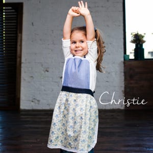 Child jumping in floral apron, kids kitchen apron for cooking and crafts.