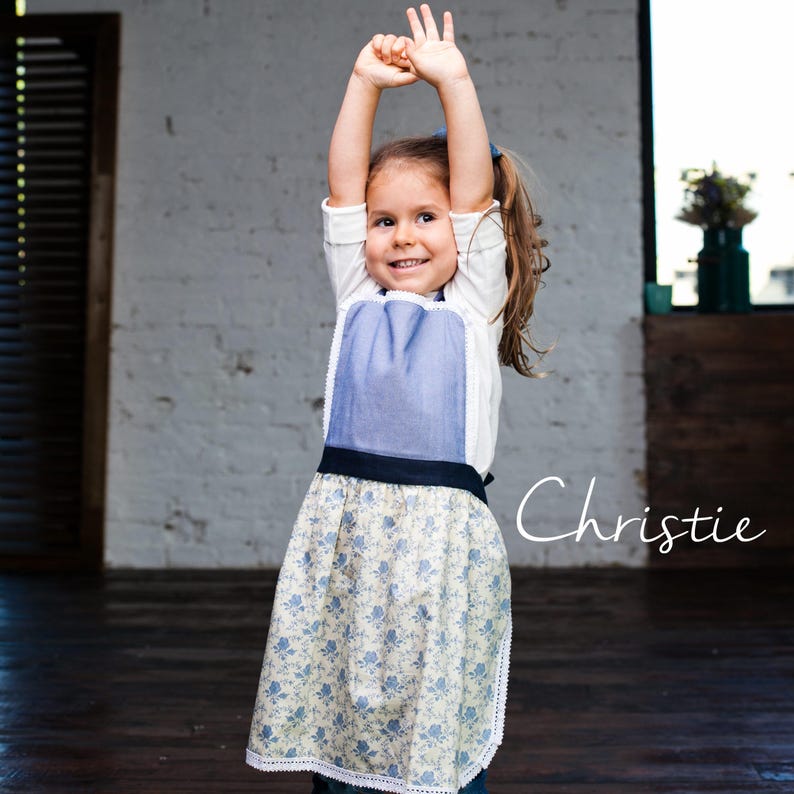 Child jumping in floral apron, kids kitchen apron for cooking and crafts.