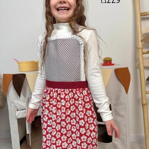 5 year old at her play kitchen wearing a grey and red kitchen apron for girls