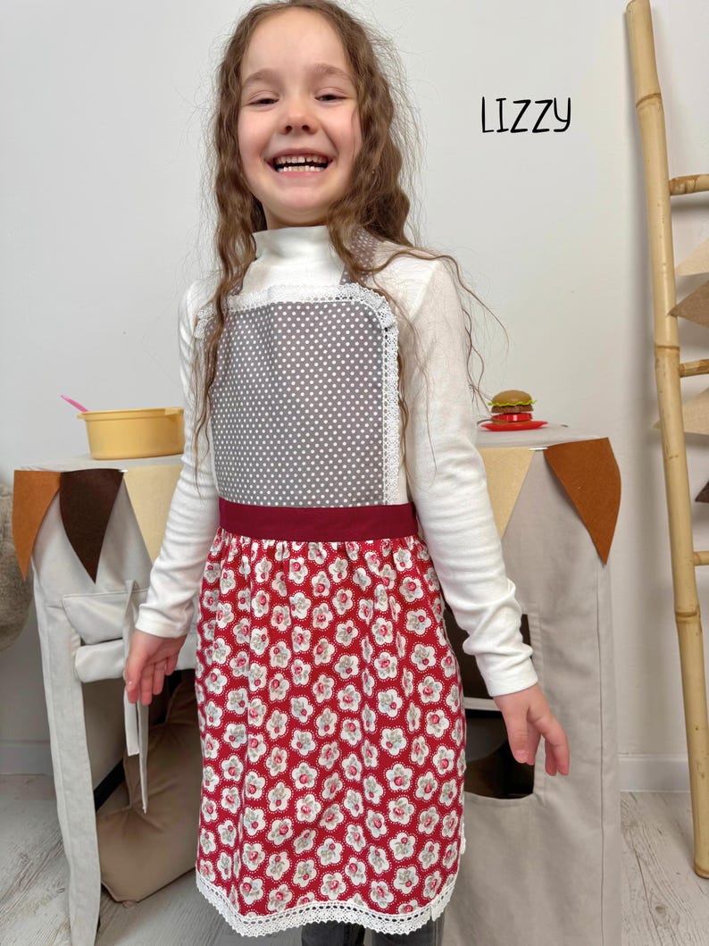 5 year old at her play kitchen wearing a grey and red kitchen apron for girls