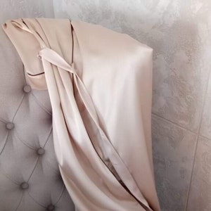 May include: A light beige satin fabric draped over a tufted headboard. The fabric is folded and tied in a knot at the top.