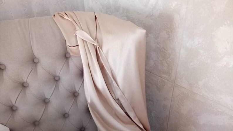 May include: A light beige satin fabric draped over a tufted headboard. The fabric is folded and tied in a knot at the top.