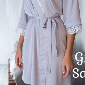 May include: A grey satin robe with white lace trim on the sleeves and a matching tie belt.