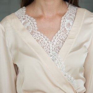 May include: A cream-colored satin robe with a white lace trim around the neckline.