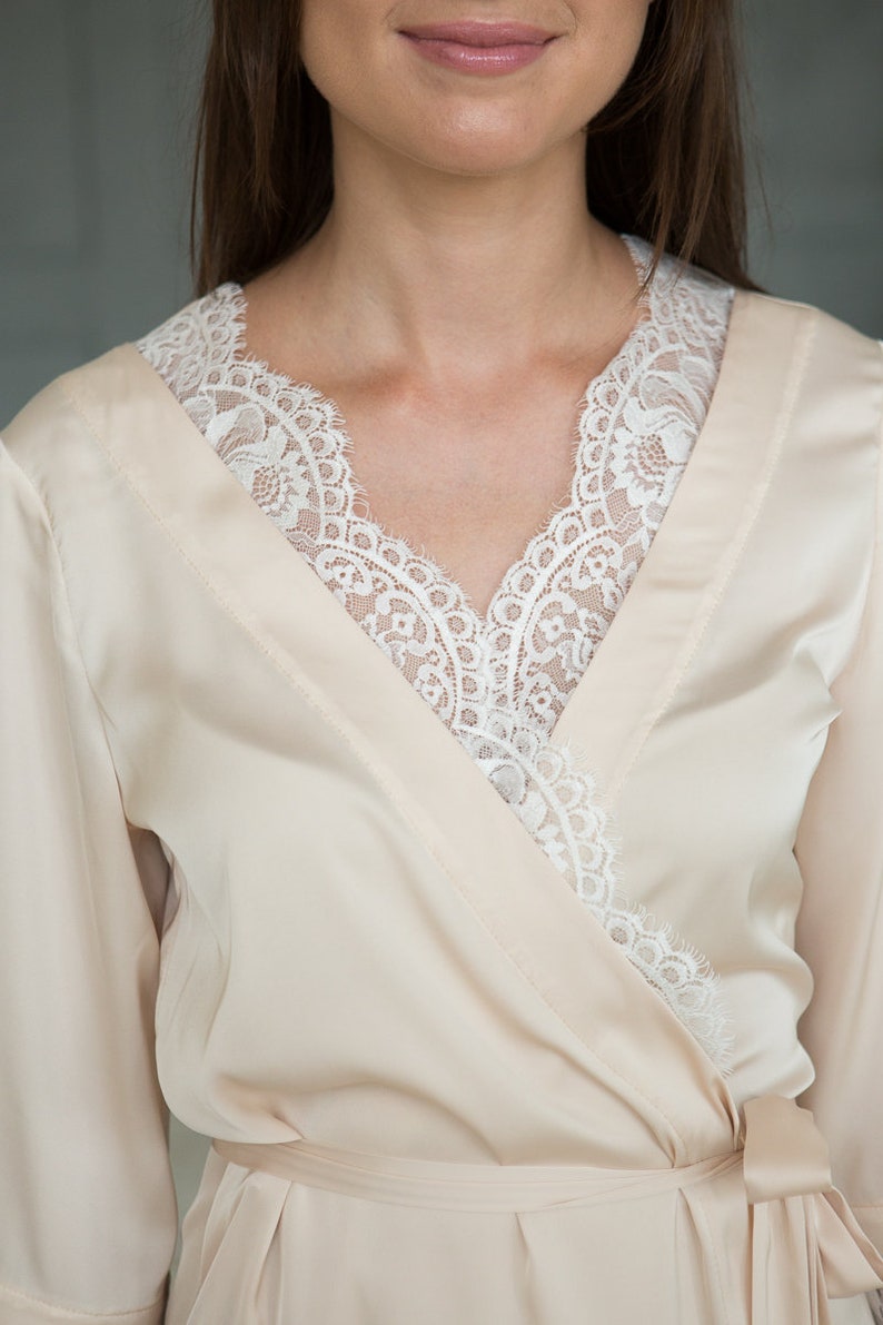 May include: A cream-colored satin robe with a white lace trim around the neckline.