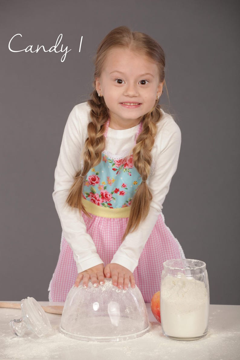 Little girl smiling and holding bowl wearing pink apron with yellow trim