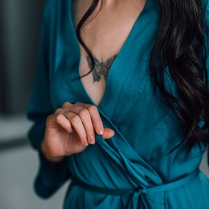 May include: A woman wearing a teal blue satin robe with a butterfly tattoo on her chest.