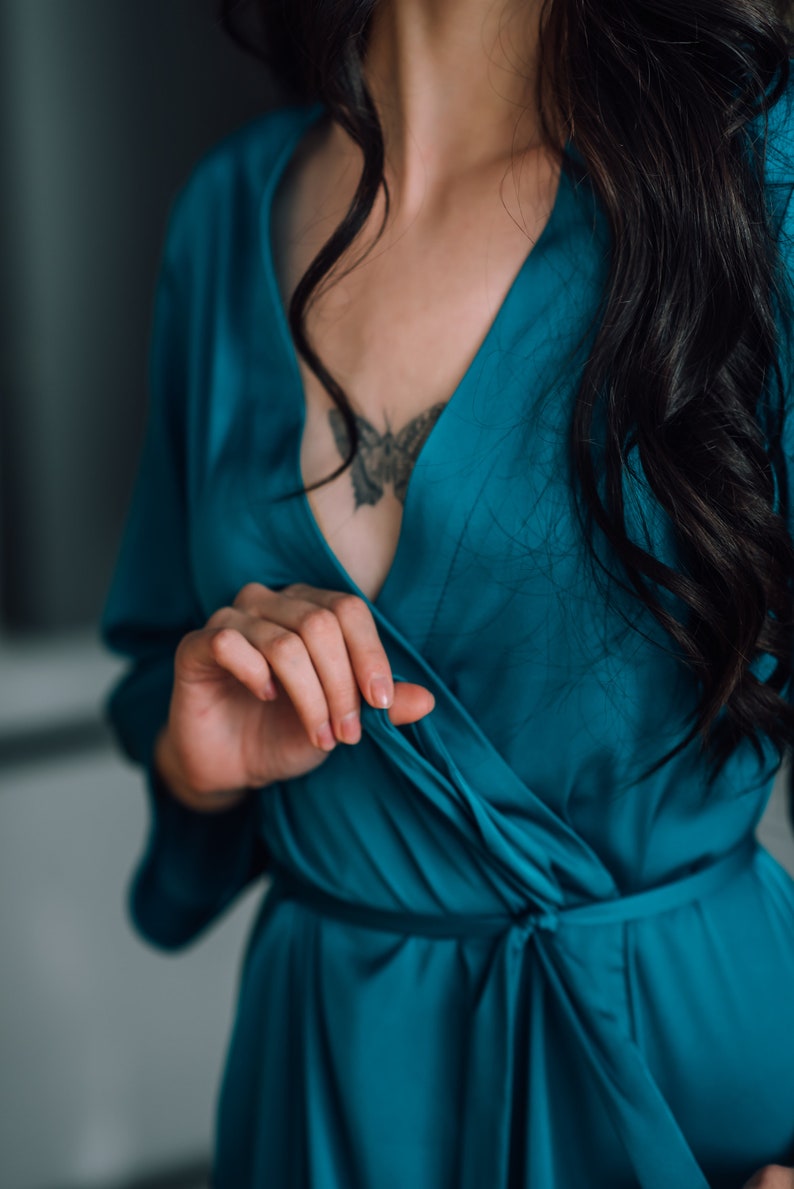 May include: A woman wearing a teal blue satin robe with a butterfly tattoo on her chest.