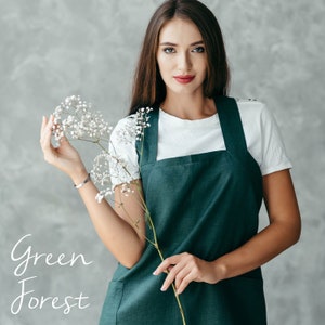 A florist wearing a green linen pinafore apron, standing in a bright studio setting.