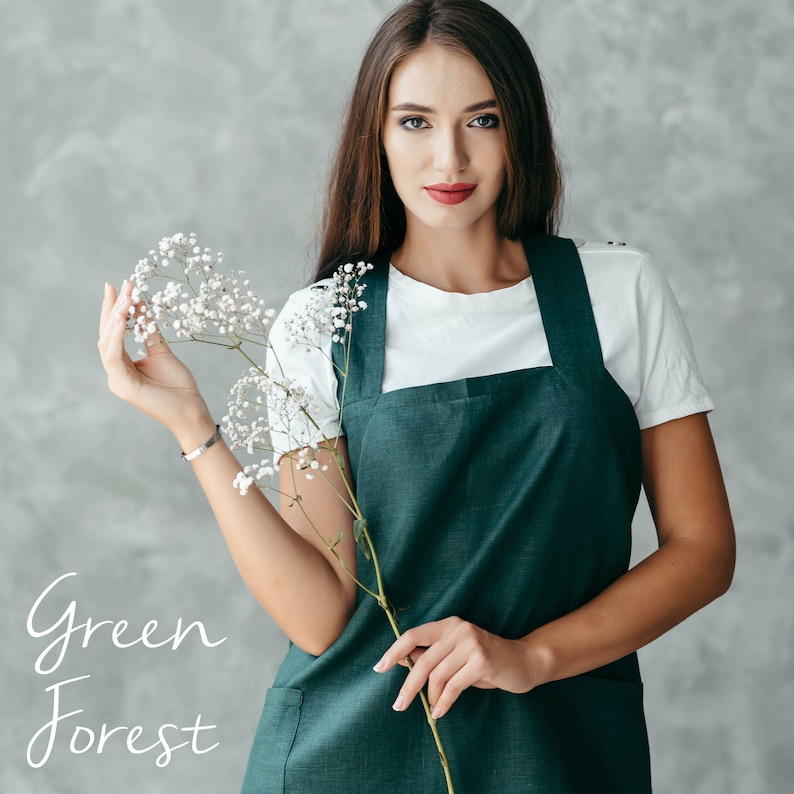 A florist wearing a green linen pinafore apron, standing in a bright studio setting.