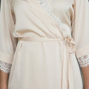 May include: A pale pink satin robe with a lace trim around the neckline and sleeves. The robe has a sash tie at the waist.