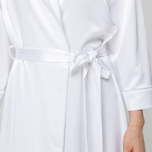 May include: A white satin robe with a self-tie sash. The robe has long sleeves and a shawl collar.