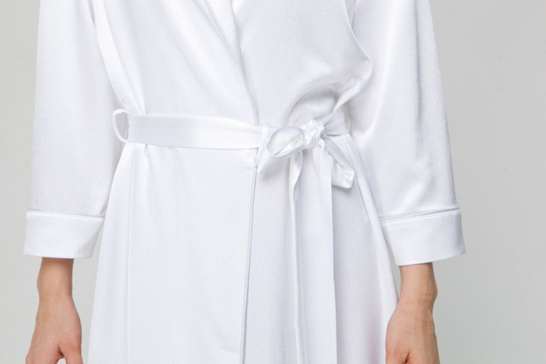 May include: A white satin robe with a self-tie sash. The robe has long sleeves and a shawl collar.