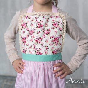 Close-up of floral bodice and pastel waistband on children’s apron, detail shot.