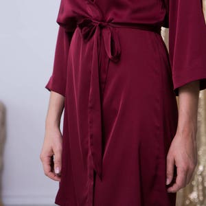 May include: A long-sleeved, burgundy satin robe with a self-tie sash. The robe is made of a soft, luxurious fabric and has a relaxed fit.