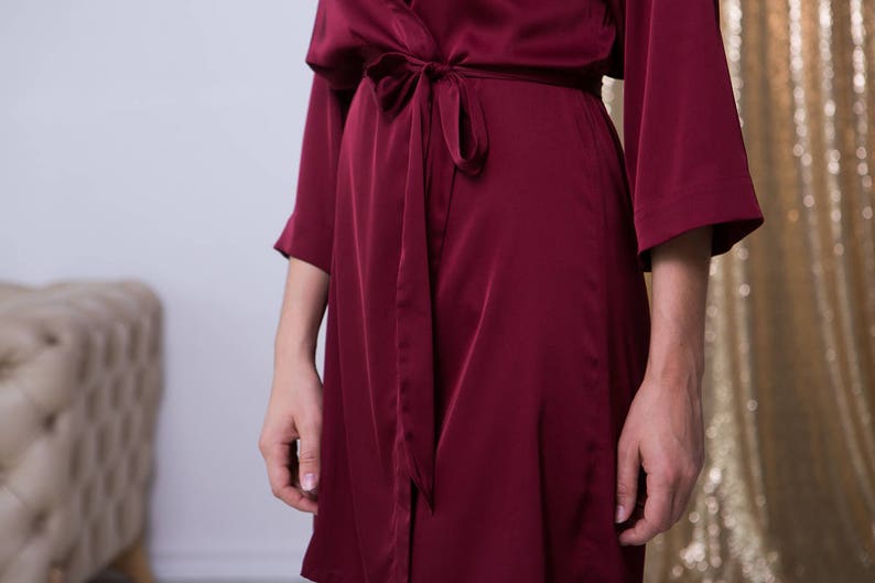 May include: A long-sleeved, burgundy satin robe with a self-tie sash. The robe is made of a soft, luxurious fabric and has a relaxed fit.