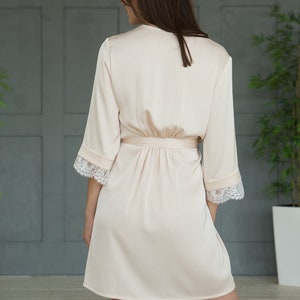 May include: A light pink satin robe with lace trim on the sleeves. The robe has a tie belt and is knee-length.