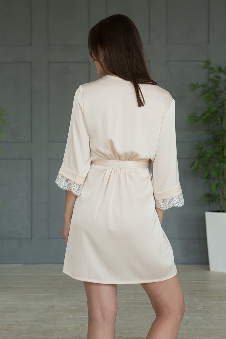 May include: A light pink satin robe with lace trim on the sleeves. The robe has a tie belt and is knee-length.