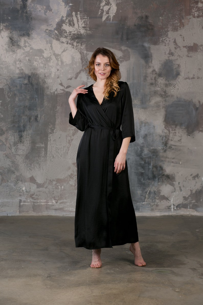 May include: A black satin robe with a long, flowing silhouette and a wrap closure. The robe has long sleeves and a V-neckline.