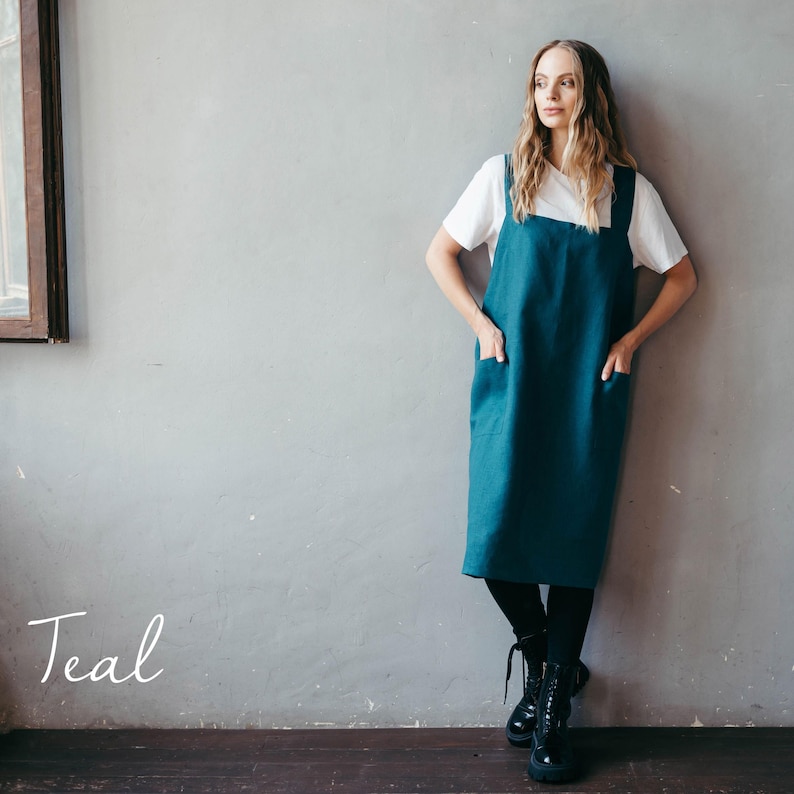 A crafter showcasing a teal linen apron, posing confidently in a sleek studio space.