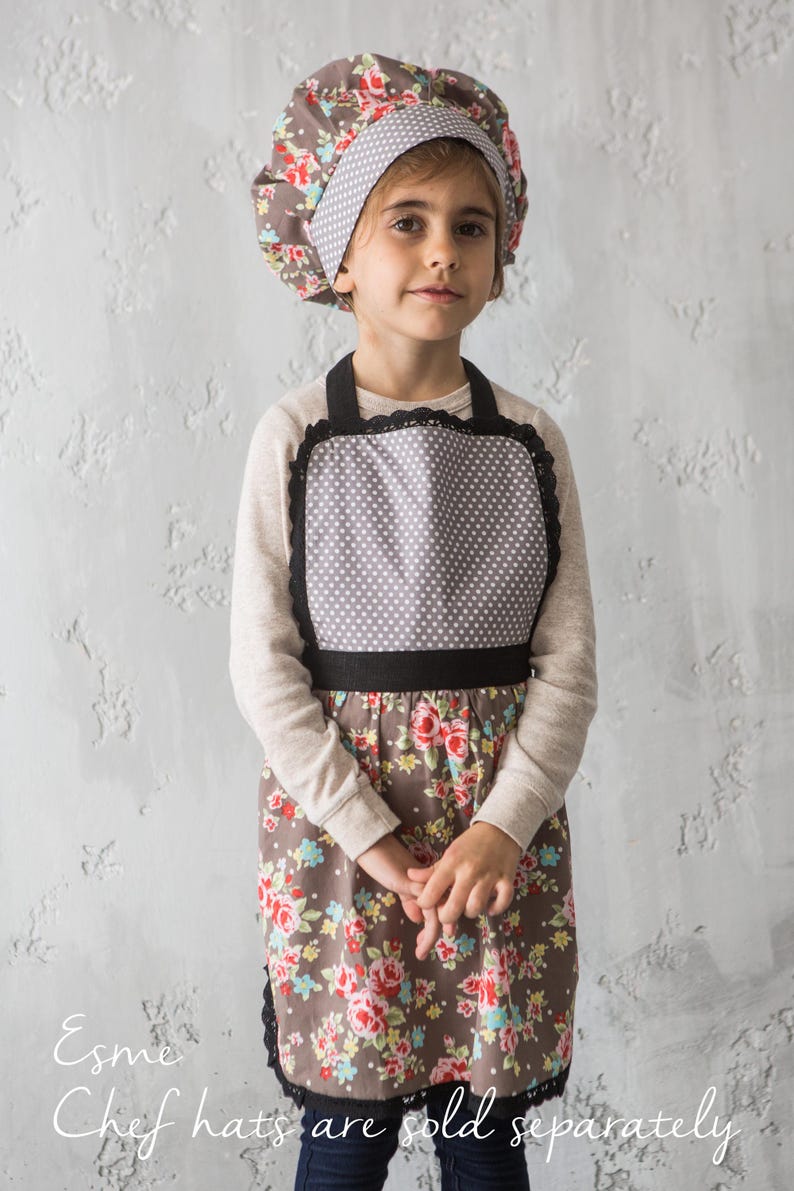 Girl in floral print apron holding whisk and wearing chef hat, family gift idea.