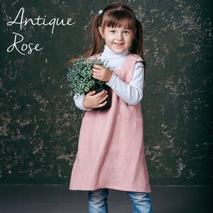 A toddler model in a soft pink apron, with its practical pockets on display.
