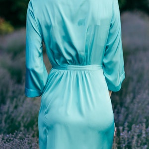 May include: A light blue satin robe with long sleeves and a tie belt. The robe is worn by a person standing in a field of lavender.