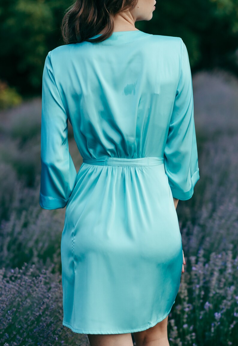 May include: A light blue satin robe with long sleeves and a tie belt. The robe is worn by a person standing in a field of lavender.