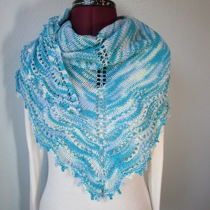 May include: A blue and white knitted shawl with a lacy border. The shawl is draped over a mannequin.